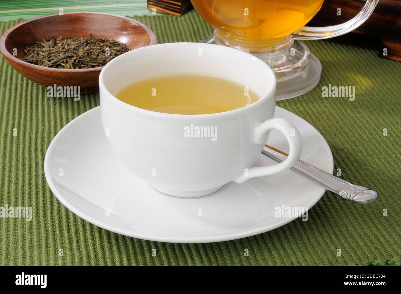 Una tazza di tè verde con foglie intere in un piatto campione Foto Stock