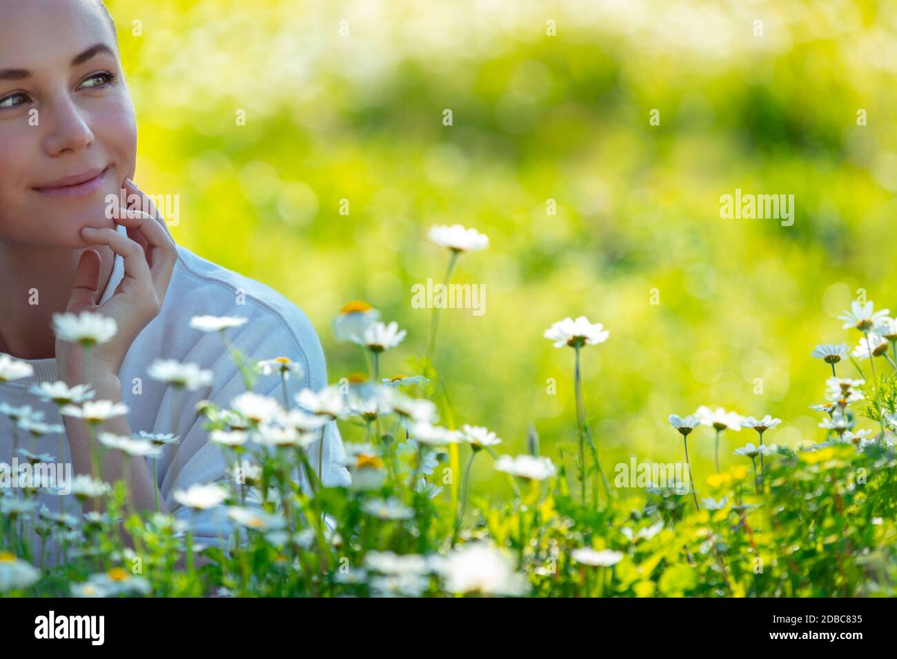 Giovane donna adagiata sull'erba fresca tra i piccoli fiori a margherita e daydreaming, godendo della bellezza e della freschezza della natura primaverile Foto Stock