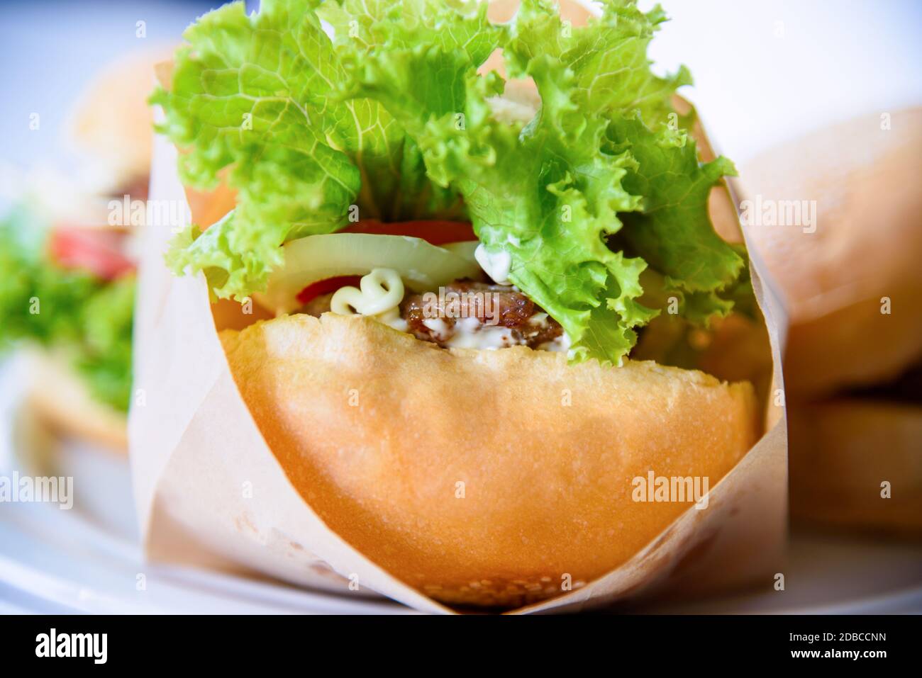 Burger è delizioso fast food americano, Closeup un hamburger a base di maiale o manzo, insalata verde di pane cipolla e pomodoro in un sacchetto di carta e piatto su t. Foto Stock