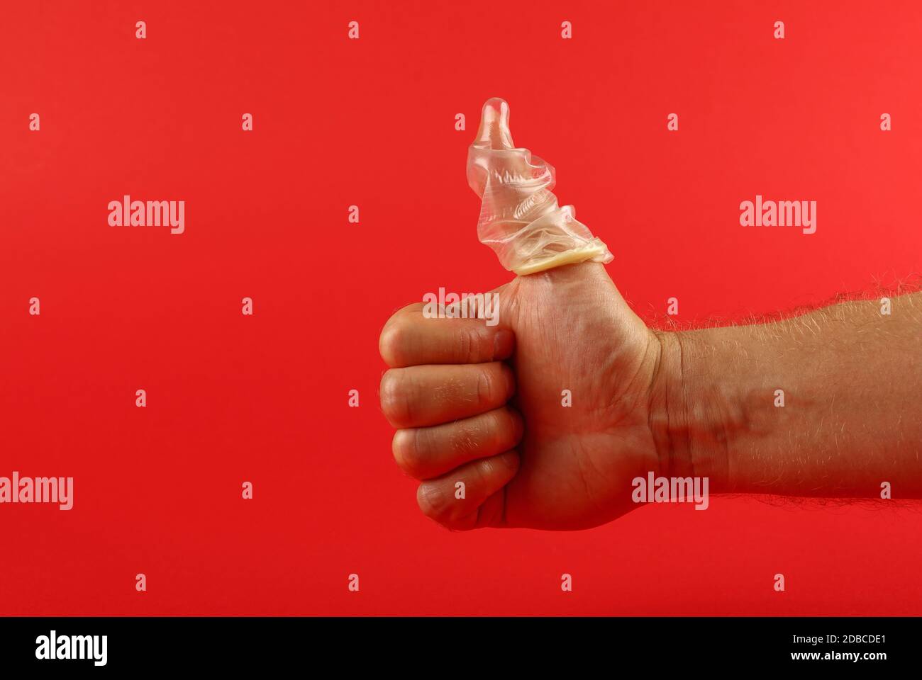 Close up man mano che mostra il pollice fino gesto con lattice preservativo sul dito su sfondo rosso con copia spazio, basso angolo vista laterale Foto Stock