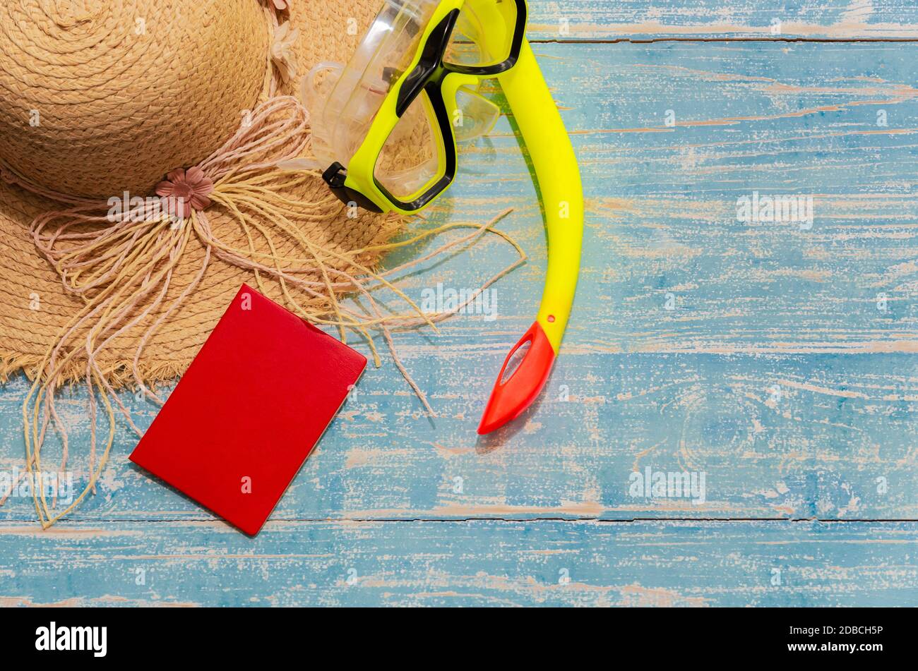Appartamento Lay estate viaggiatore accessori di cappello di paglia spiaggia, snorkeling giallo e passaporto rosso su sfondo di legno blu. Vacanza estiva e concetto di viaggio Foto Stock