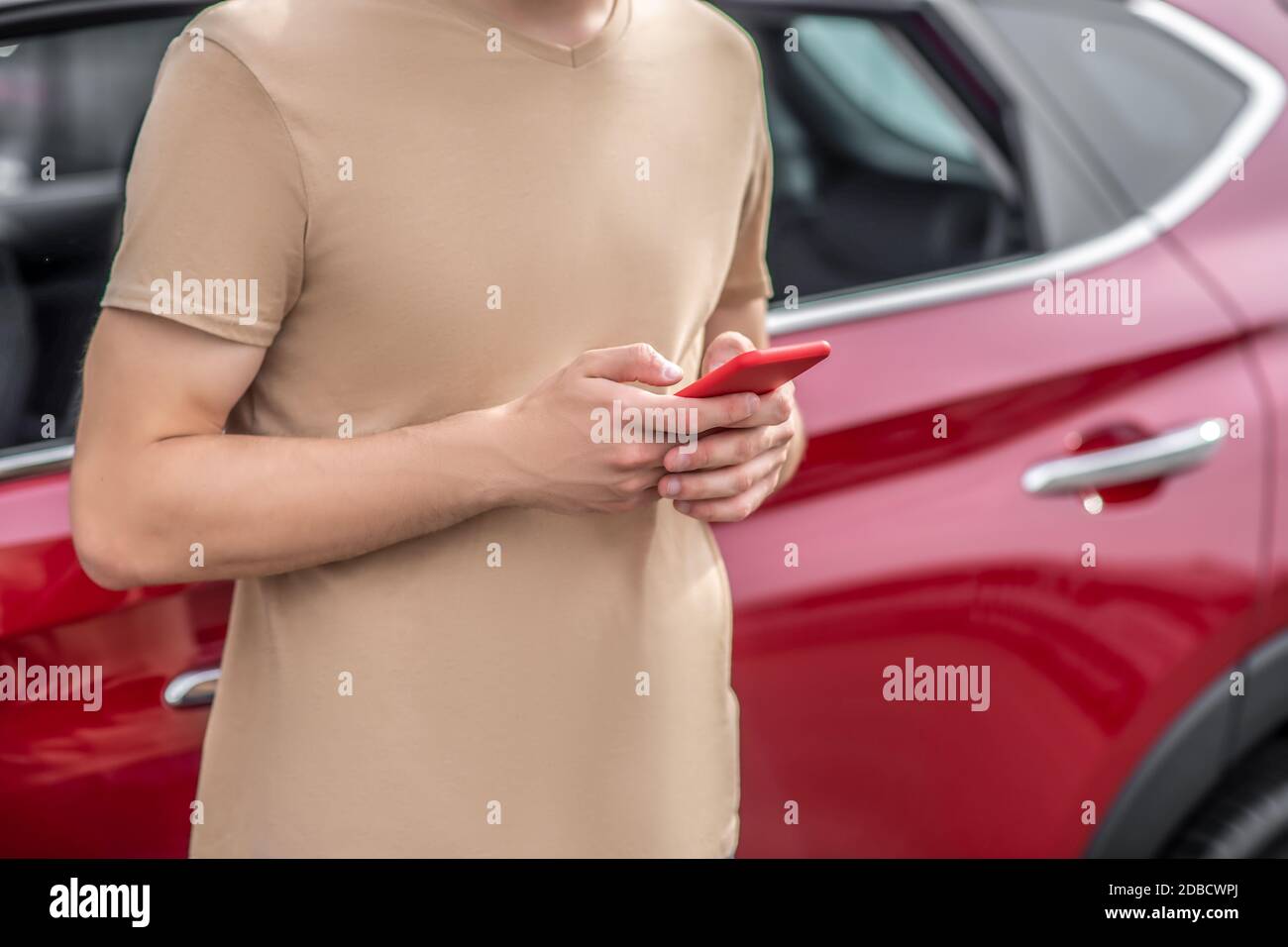 Primo piano delle mani maschili che tengono lo smartphone davanti al rosso auto Foto Stock