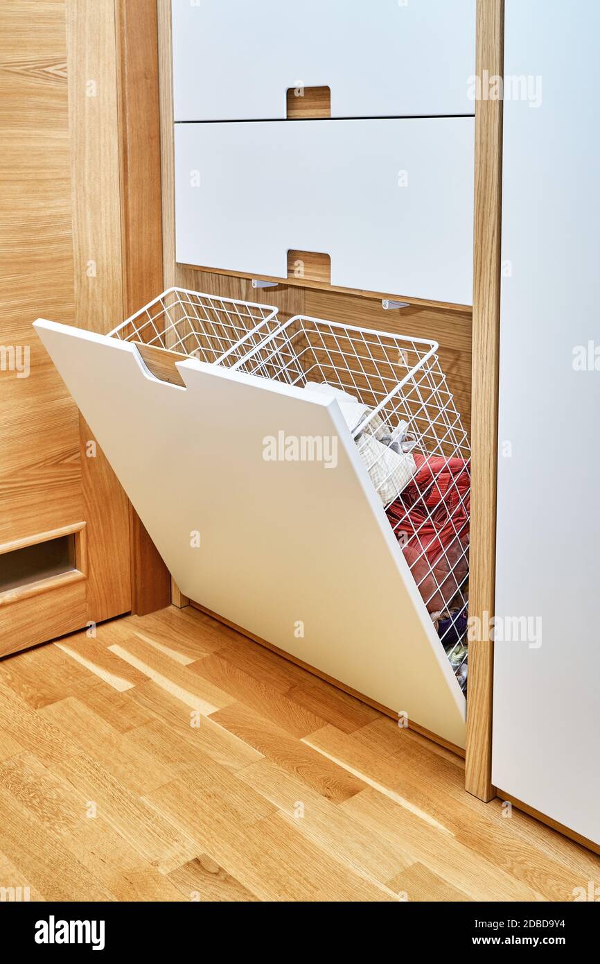 armadio moderno con cesto di bucato in mesh di metallo aperto. armadio in legno con ante per armadio a scomparsa. Mobili in legno compensato di quercia con luce Foto Stock