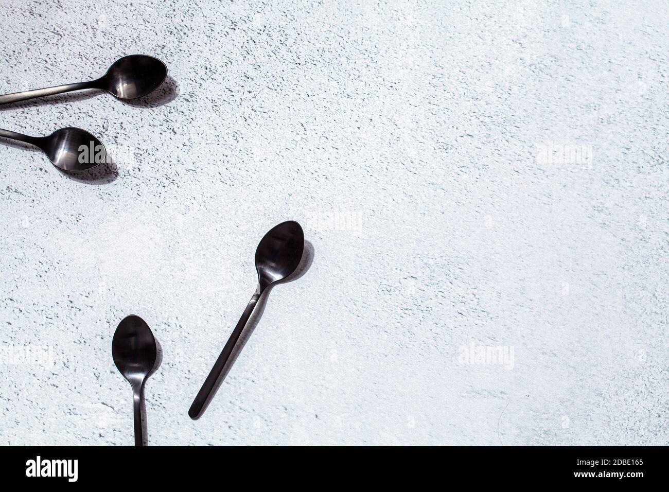 Svuotare i cucchiai da dessert neri su sfondo grigio, spazio per la copia. Mangiare cibo concetto. Foto Stock