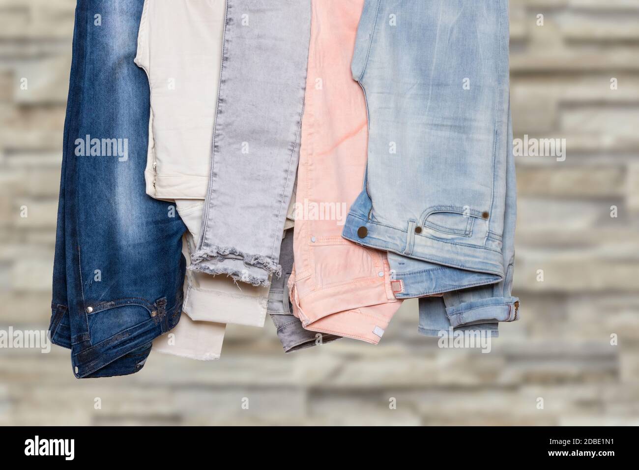 Primo piano della collezione di cinque pantaloni denim femmina vari o  pantaloni colorati su una ringhiera contro la parete di cemento grigio  chiaro sfocato. Jeans moda Foto stock - Alamy