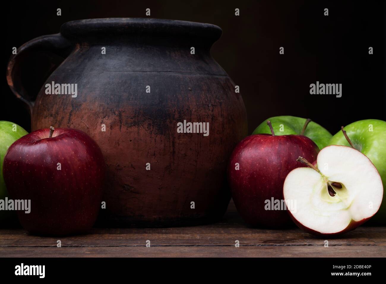 Mele rosse e verdi con vecchia caraffa in ceramica. Inquadratura a livello degli occhi con un'atmosfera rustica scura. Foto Stock