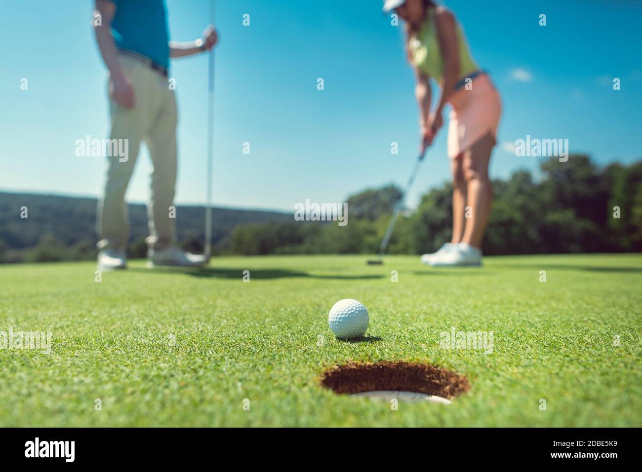 Accoppia giocando a golf con la donna su green a hole mentre il suo partner sta guardando Foto Stock