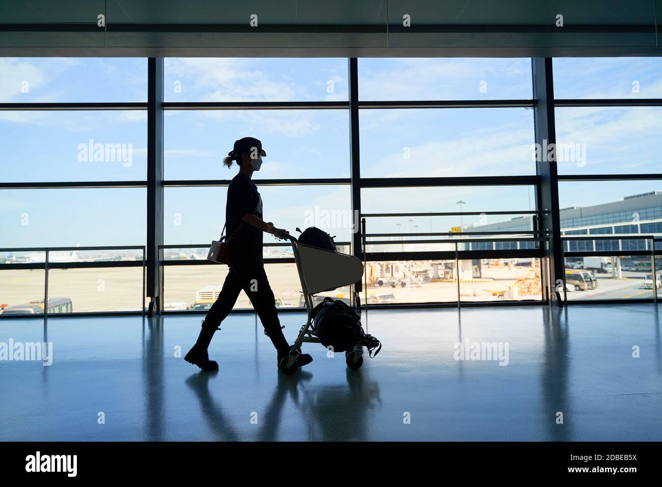 silhouette di una donna asiatica viaggiatore d'aria femminile che cammina spingendo un carrello nell'edificio del terminal dell'aeroporto Foto Stock