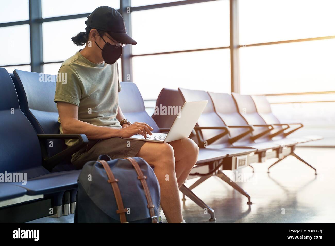 uomo asiatico viaggiatore d'aria maschile con maschera nera seduta nell'area d'attesa emply nell'edificio del terminal dell'aeroporto usando il laptop computer Foto Stock