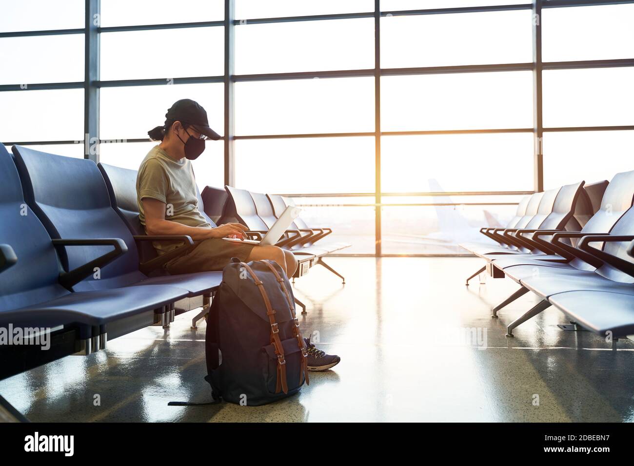 uomo asiatico viaggiatore d'aria maschile con maschera nera seduta nell'area d'attesa emply nell'edificio del terminal dell'aeroporto usando il laptop computer Foto Stock