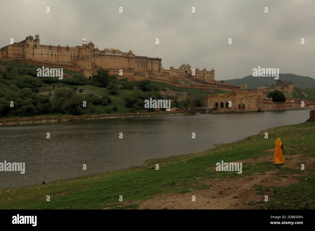 Una donna in abito da lavoro che cammina sul lato del lago Maota, che domina lo storico Forte Amer ad Amer, Rajasthan, India. Foto Stock