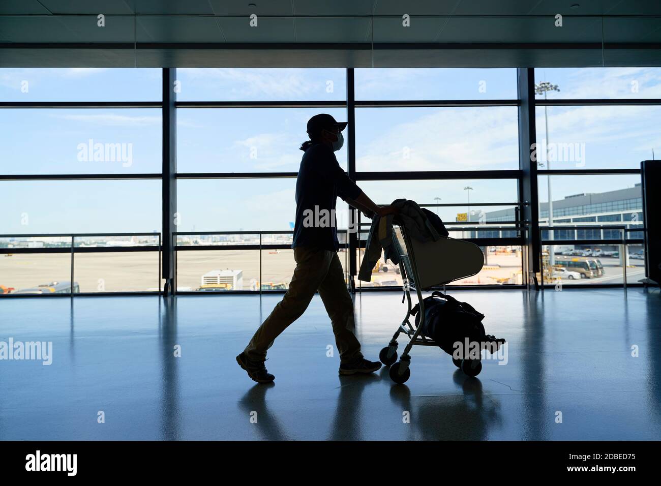 silhouette di un uomo asiatico maschile viaggiatore d'aria che cammina spingendo un carrello nell'edificio del terminal dell'aeroporto Foto Stock