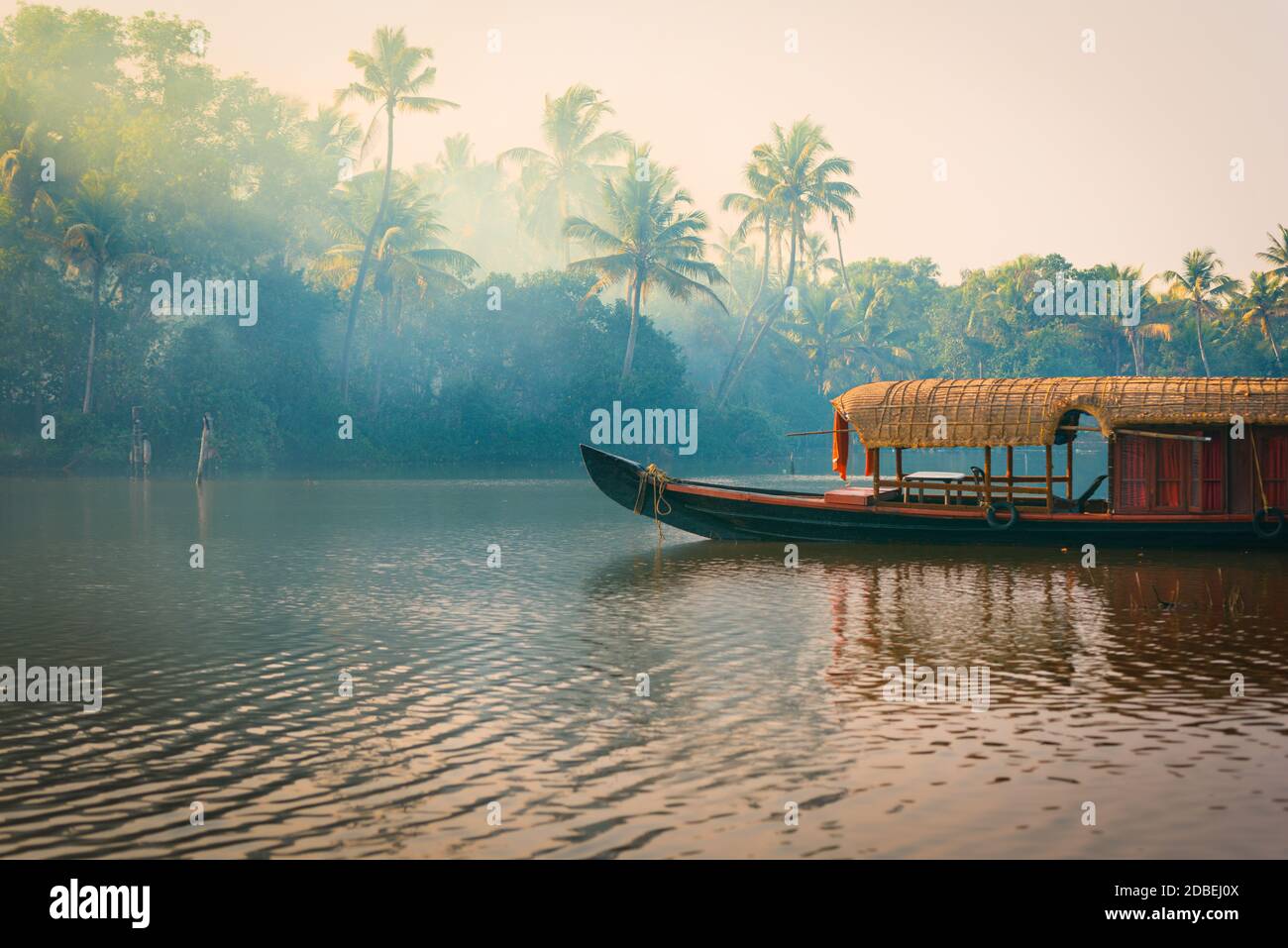 Una tradizionale casa barca è ancorata sulle rive di un lago di pesca nella giungla di palme al tramonto, nel Backwaters, una destinazione popolare per y Foto Stock