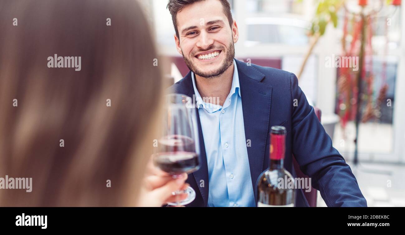 Uomo e donna che gustano un bicchiere di vino rosso con il loro pasto avendo un grande tempo Foto Stock