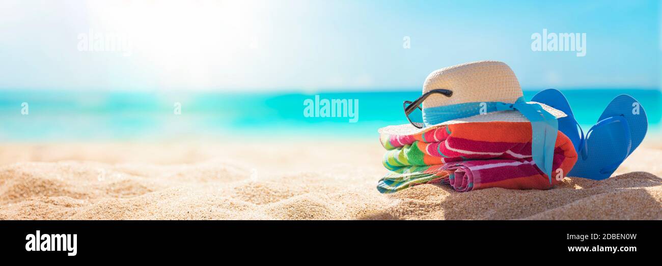 Accessori spiaggia cappello di paglia, infradito, asciugamano sulla soleggiata spiaggia tropicale, vacanze estive, spiaggia caraibica con sfondo di acqua turchese Foto Stock