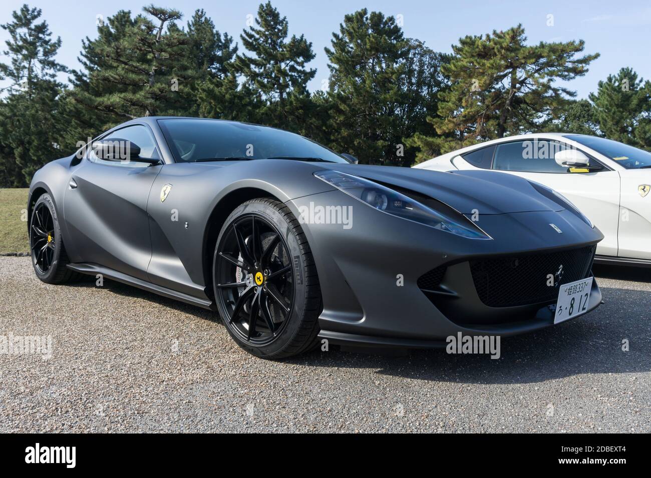 Vista frontale di una Ferrari 812 Superfast nero opaco con cerchi da corsa neri forgiati da 20 pollici all'esterno in un parco al sole Foto Stock