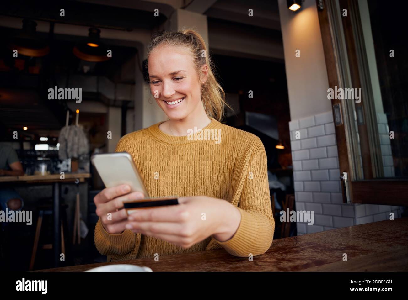 Donna felice in caffè che effettua il pagamento online utilizzando la carta e. smartphone nel bar Foto Stock