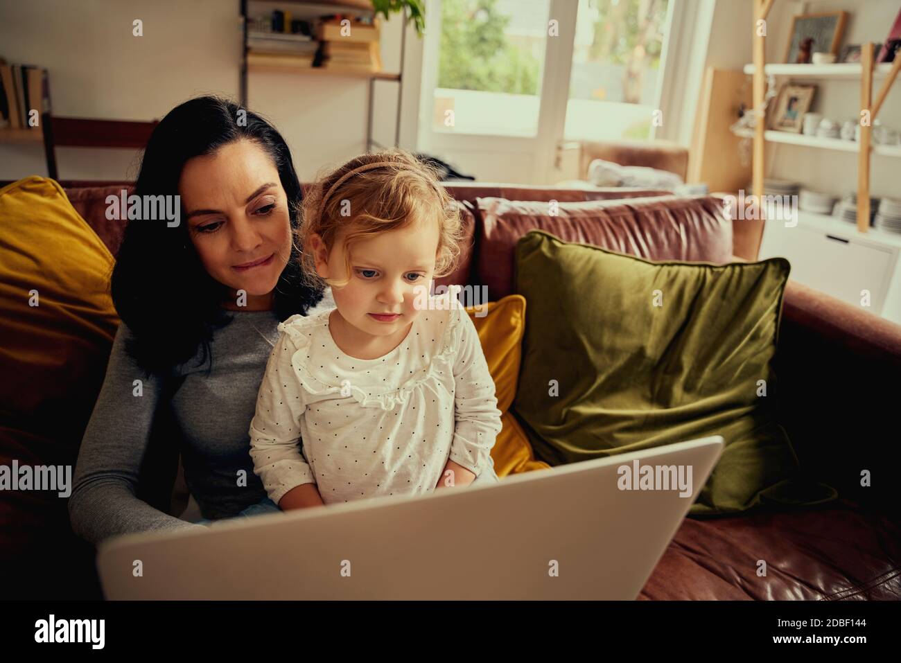 Giovane madre e figlia di capretto che hanno shopping divertente in linea usando computer portatile seduto sul divano Foto Stock