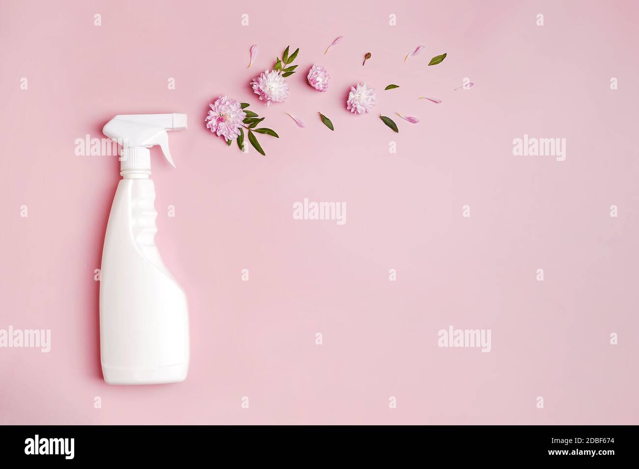 Bottiglia di plastica con spray detergente e fiori su sfondo rosa. Foto Stock