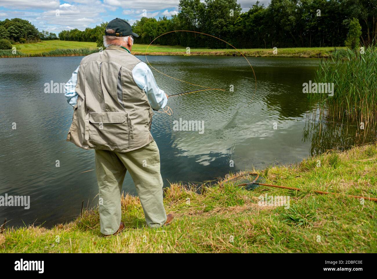 Lincolnshire, Regno Unito - il sig. Barry Grantham, un istruttore nella pesca della mosca, che getta una linea di mosca attraverso un lago della trota per la trota iridea Foto Stock