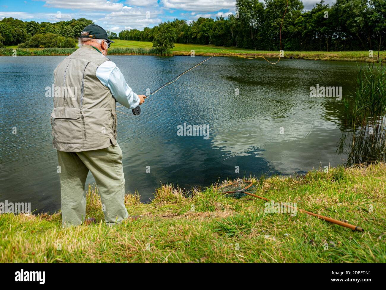 Lincolnshire, Regno Unito - il sig. Barry Grantham, un istruttore nella pesca della mosca, che getta una linea di mosca attraverso un lago della trota per la trota iridea Foto Stock