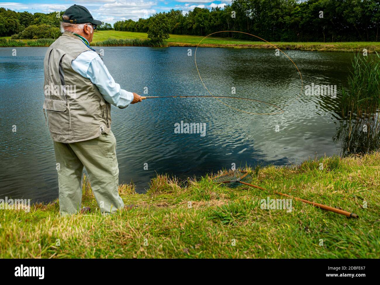 Lincolnshire, Regno Unito - il sig. Barry Grantham, un istruttore nella pesca della mosca, che getta una linea di mosca attraverso un lago della trota per la trota iridea Foto Stock