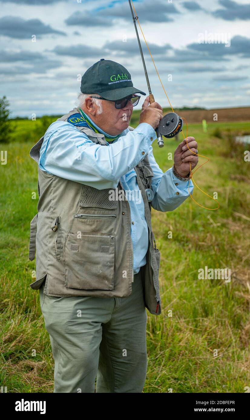 Lincolnshire, Regno Unito - il sig. Barry Grantham, un istruttore nella pesca della mosca, che getta una linea di mosca attraverso un lago della trota per la trota iridea Foto Stock