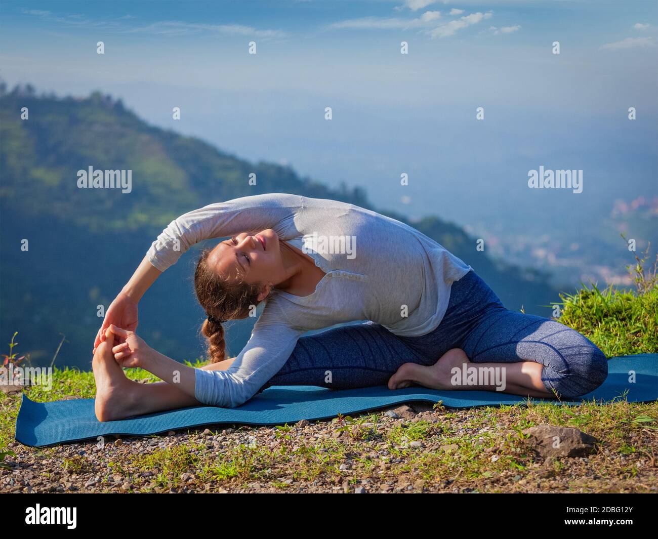 Yoga Outdoors - giovane donna sportiva che fa Hatha Yoga Asana parivrtta janu sirsasana - Revoluto posizione testa-ginocchio - in montagne al mattino Foto Stock