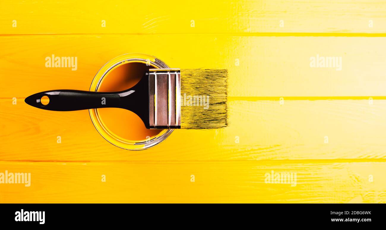 Banner fatto con lattino aperto di vernice gialla con pennello su di esso. Sfondo di legno giallo dipinto di fresco. Foto Stock