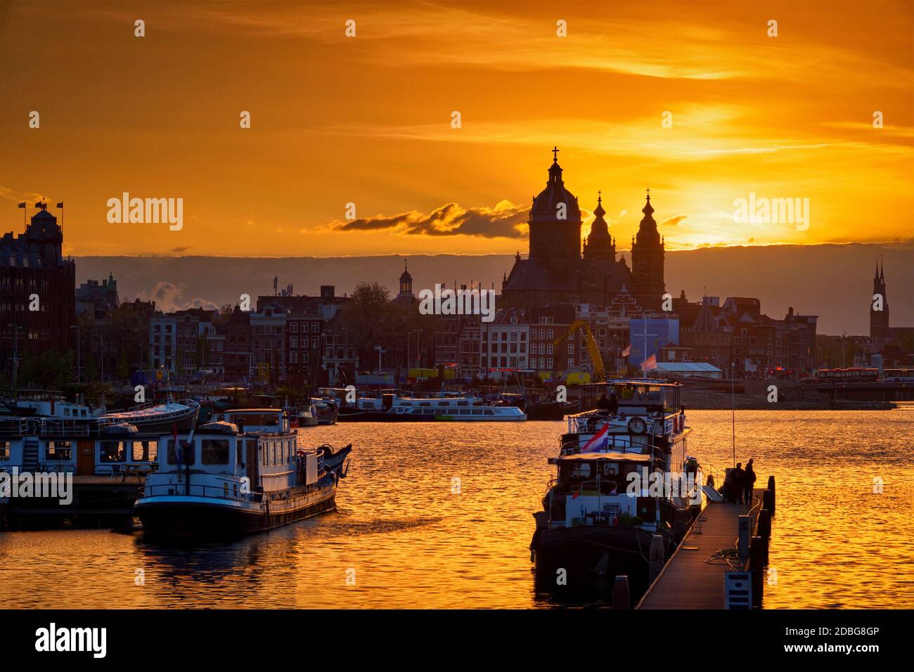 Skyline di Amsterdam con la Chiesa di San Nicola (Sint-Nicolaaskerk) e barche sul molo al tramonto con il cielo drammatico. Amsterdam, Paesi Bassi Foto Stock