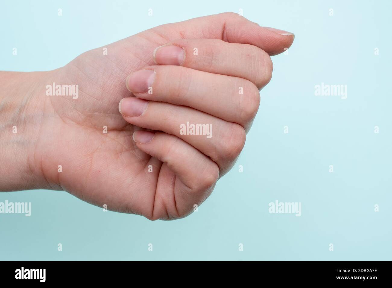 Concetto per unghie naturali, unghie grezze. Primo piano di una mano femmina caucasica con unghie naturali non lucidate, cuticola sopravfatta su sfondo blu, top v Foto Stock