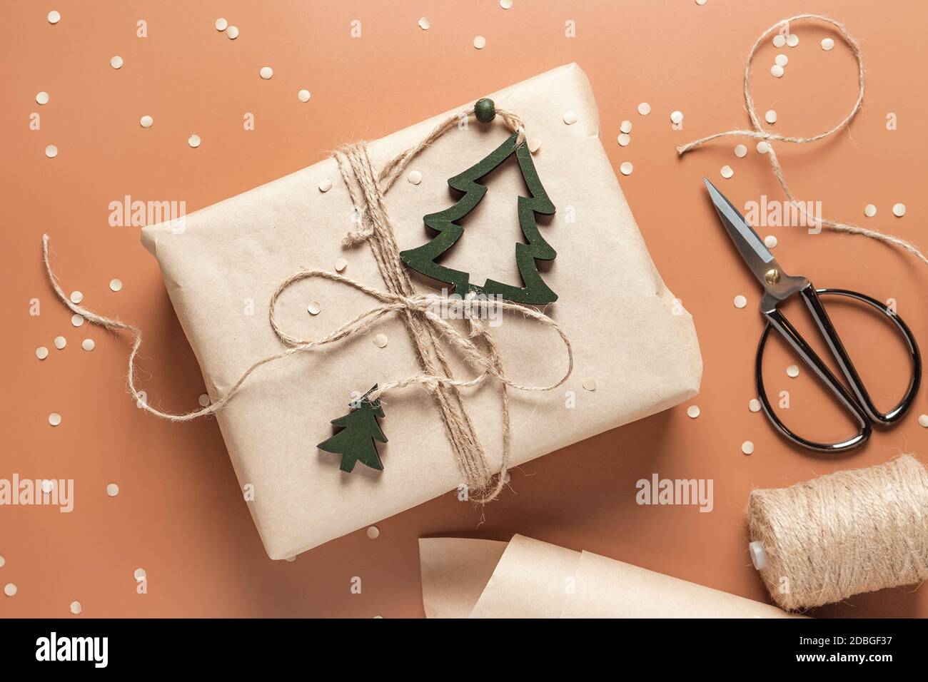 Confezione regalo in carta artigianale su sfondo marrone caramello, forbici e carta da imballaggio nelle vicinanze. Il concetto di preparazione per la vacanza. Vista dall'alto Foto Stock