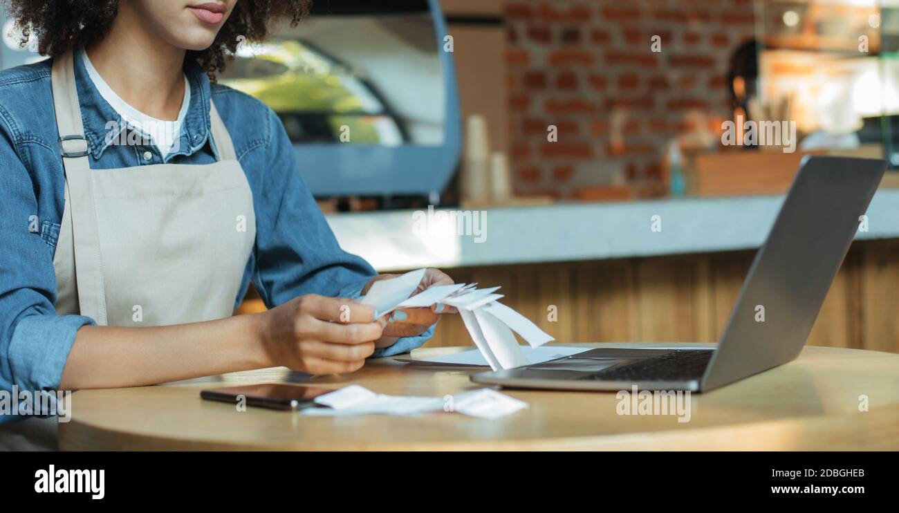 Millennial afroamericano donna proprietario manager in grembiule lavora con conto e contabilità in caffè, panorama, ritagliato Foto Stock