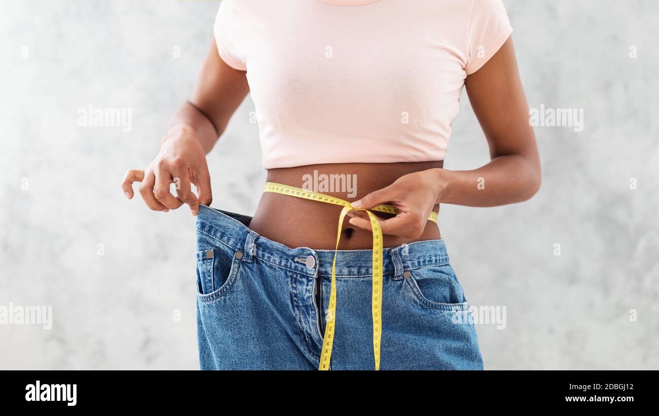 Donna nera in vecchi jeans grandi che misura la sua vita, mostrando  risultati di dieta dimagrante o liposuzione, sfondo grigio Foto stock -  Alamy