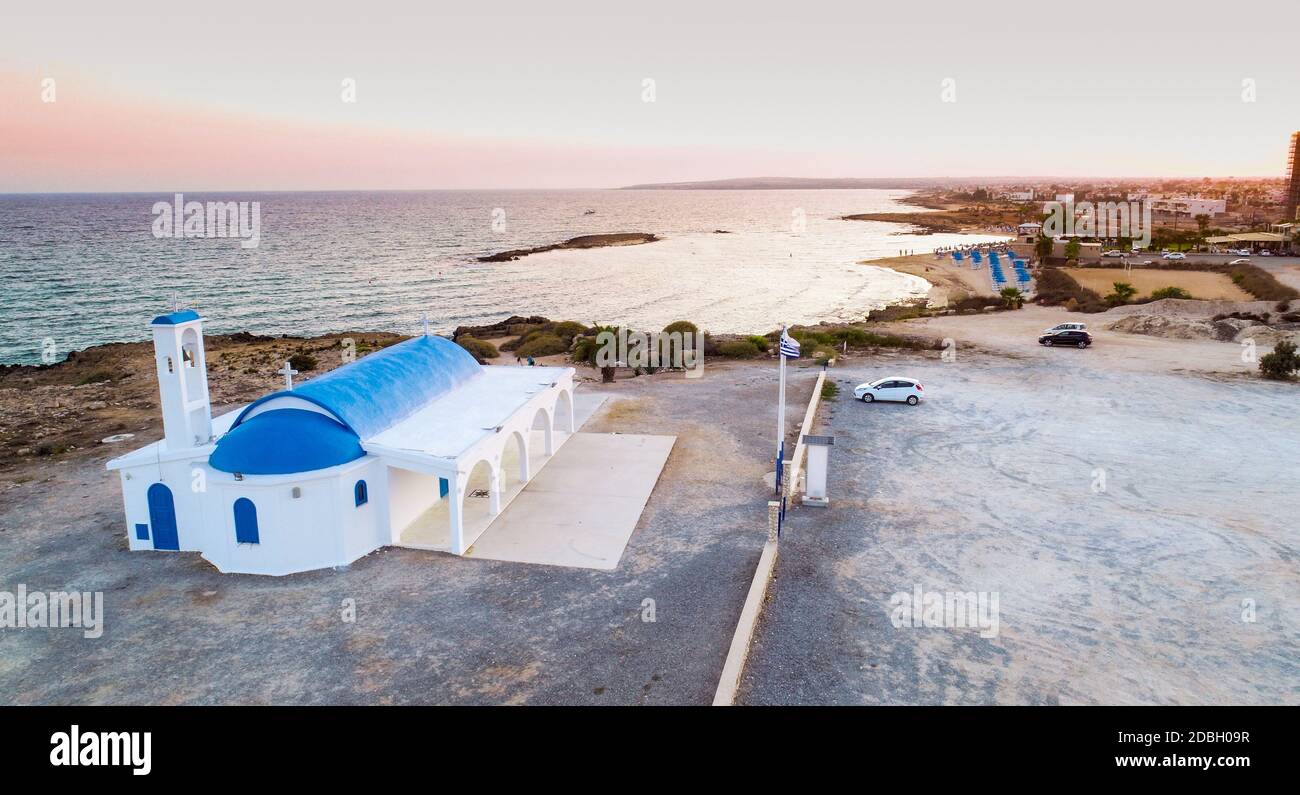 Vista aerea del tramonto sulla costa e tradizionale cappella dipinta di bianco con porte blu sulla spiaggia di Agia Thekla, Ayia Napa, Famagosta, Cipro da A. Foto Stock