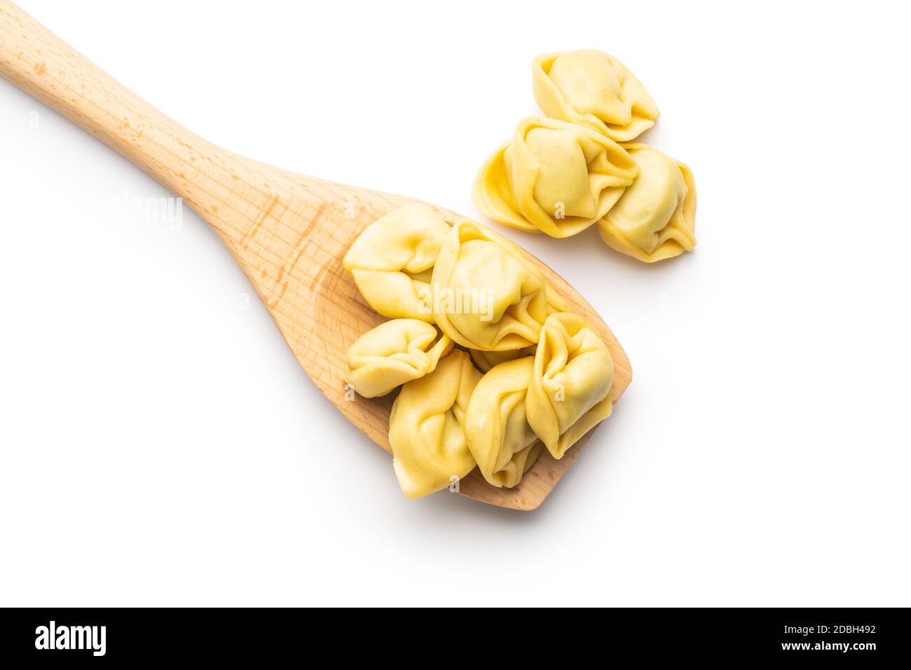 Tortellini su cucchiaio di legno. Pasta ripiena italiana isolata su sfondo bianco. Foto Stock