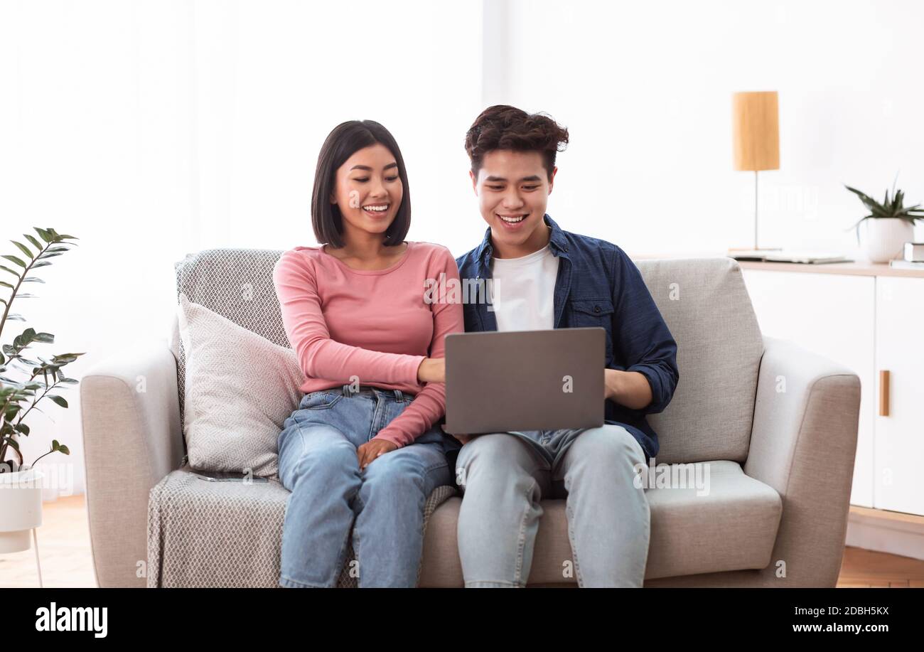 I coniugi giapponesi che usano il computer portatile seduto sul divano nel soggiorno Foto Stock
