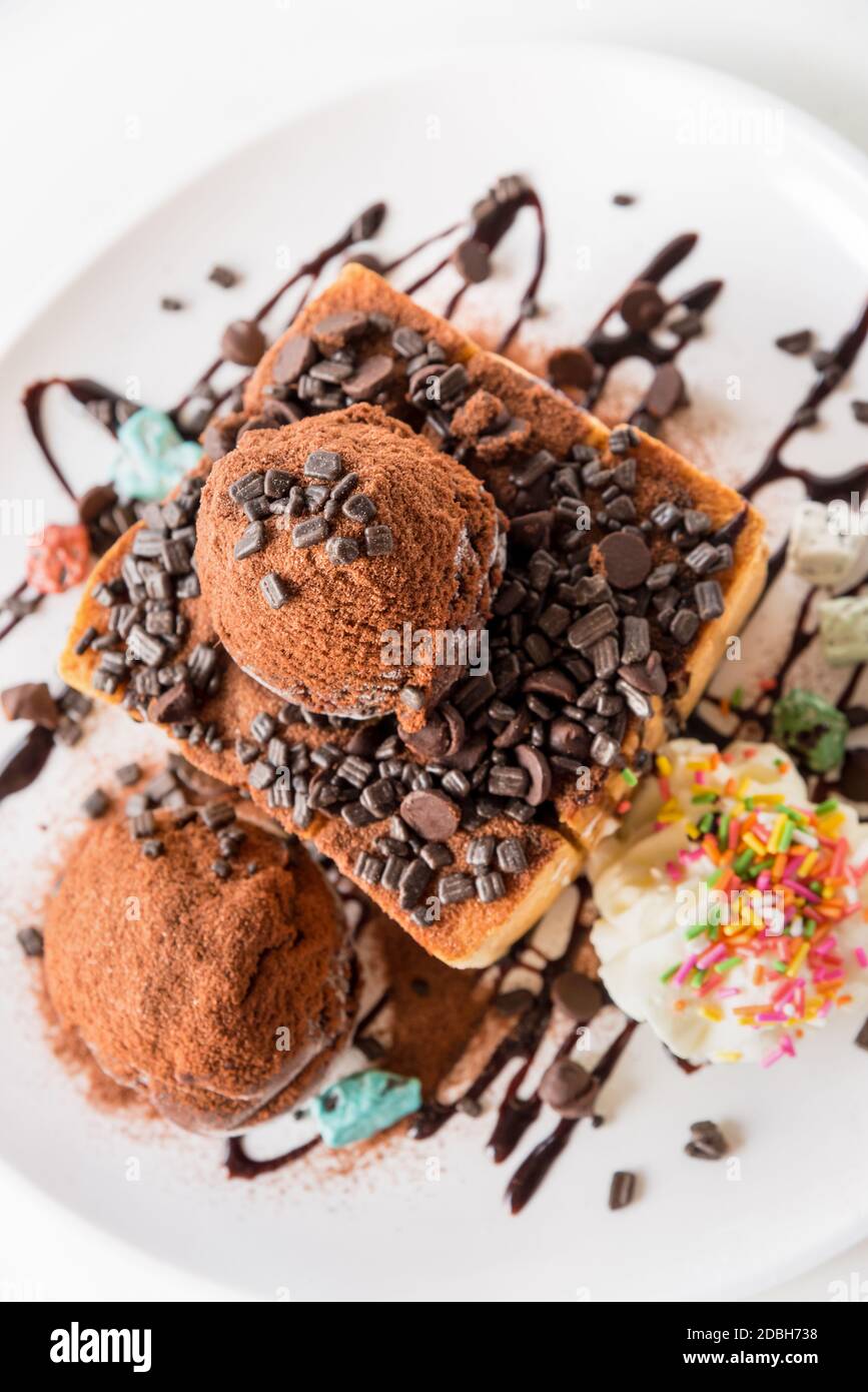Primo piano vista dall'alto pane al Miele e paletta per gelato al cioccolato con sciroppo decorare con una pastiglia di cioccolato in un piatto bianco sul tavolo Foto Stock
