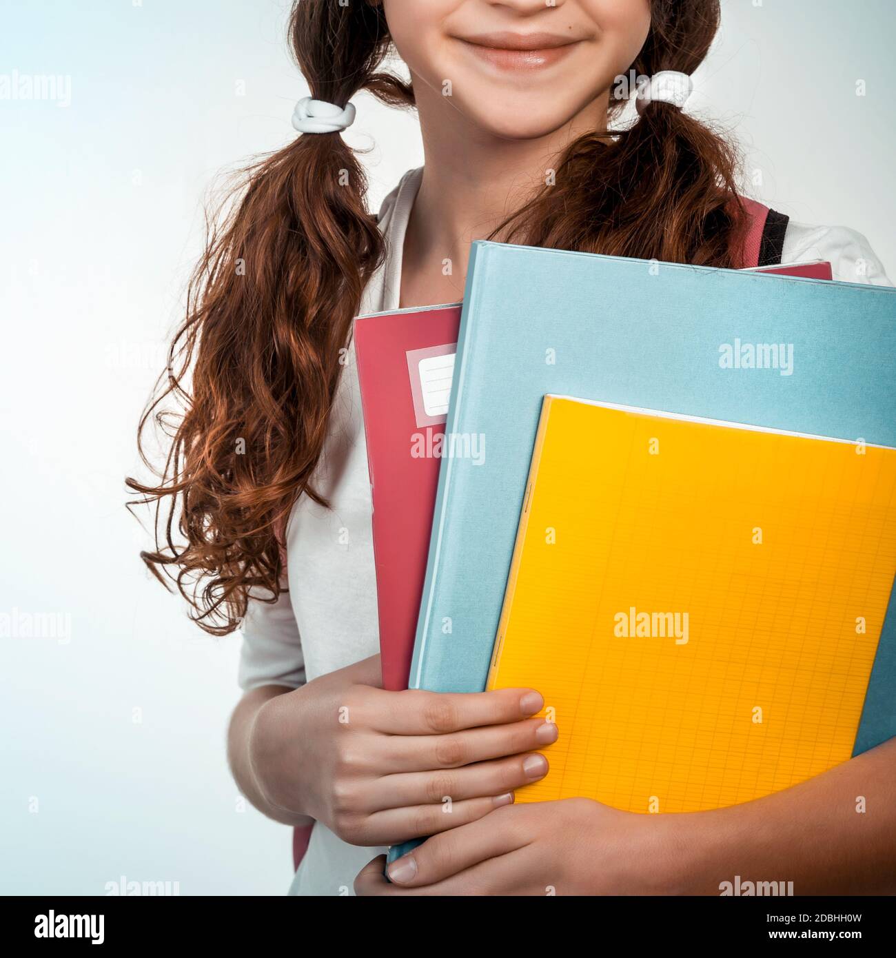 Ritratto di carina bruna scolastica tenendo in mano tre taccuini colorati, parte viso, isolato su sfondo chiaro, concetto di ritorno a scuola Foto Stock