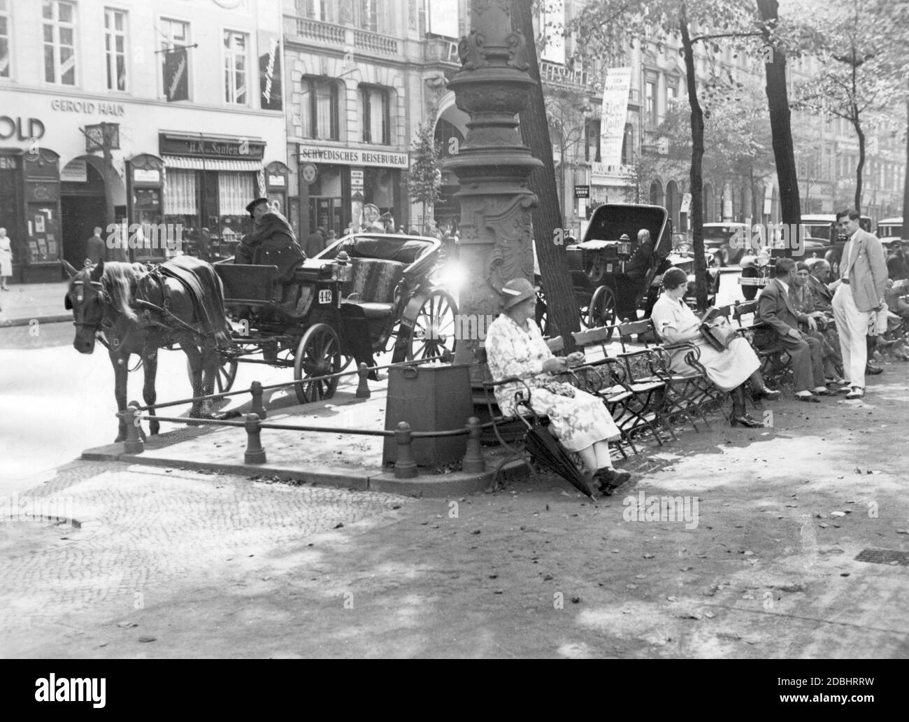 'I pedoni siedono sulle sedie all'ombra sulla strada Unter den Linden a Berlino. Sullo sfondo, la casa Gerold con il negozio di ''H. N. van Santen'', una 'Agenzia di Viaggi Swedish' e il cinema ''Passage-Lichtspiele'' nella Kaisergalerie. La foto è stata scattata nel 1932 dal fotografo Herbert Hoffmann." Foto Stock