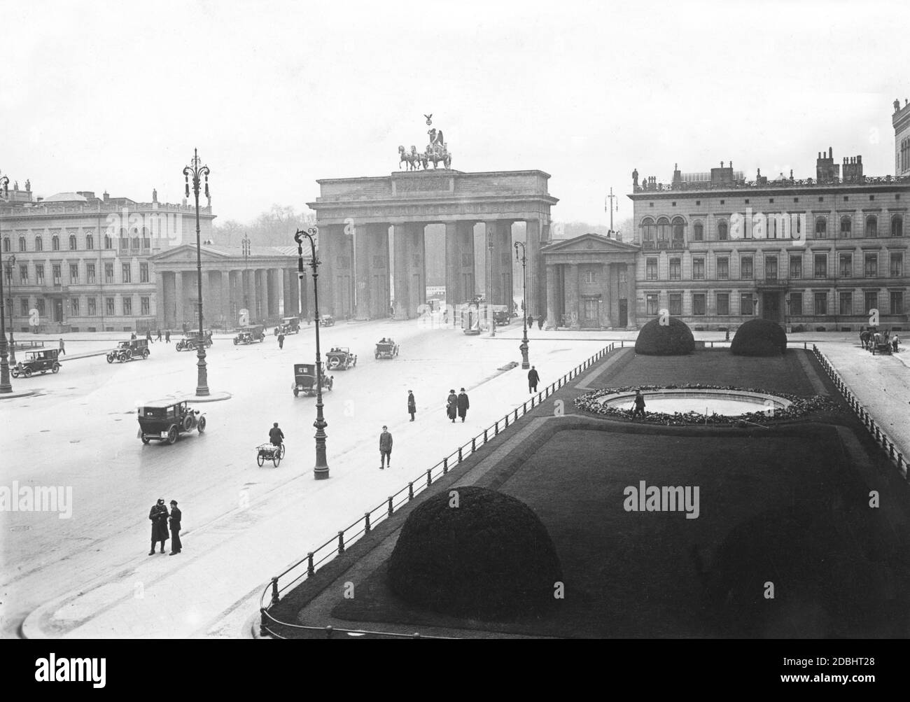 Il traffico in auto passa sulla Pariser Platz e attraverso la porta di Brandeburgo a Berlino. Sulla destra, un giardiniere tende lo spazio verde. La foto è stata scattata negli anni venti. Foto Stock