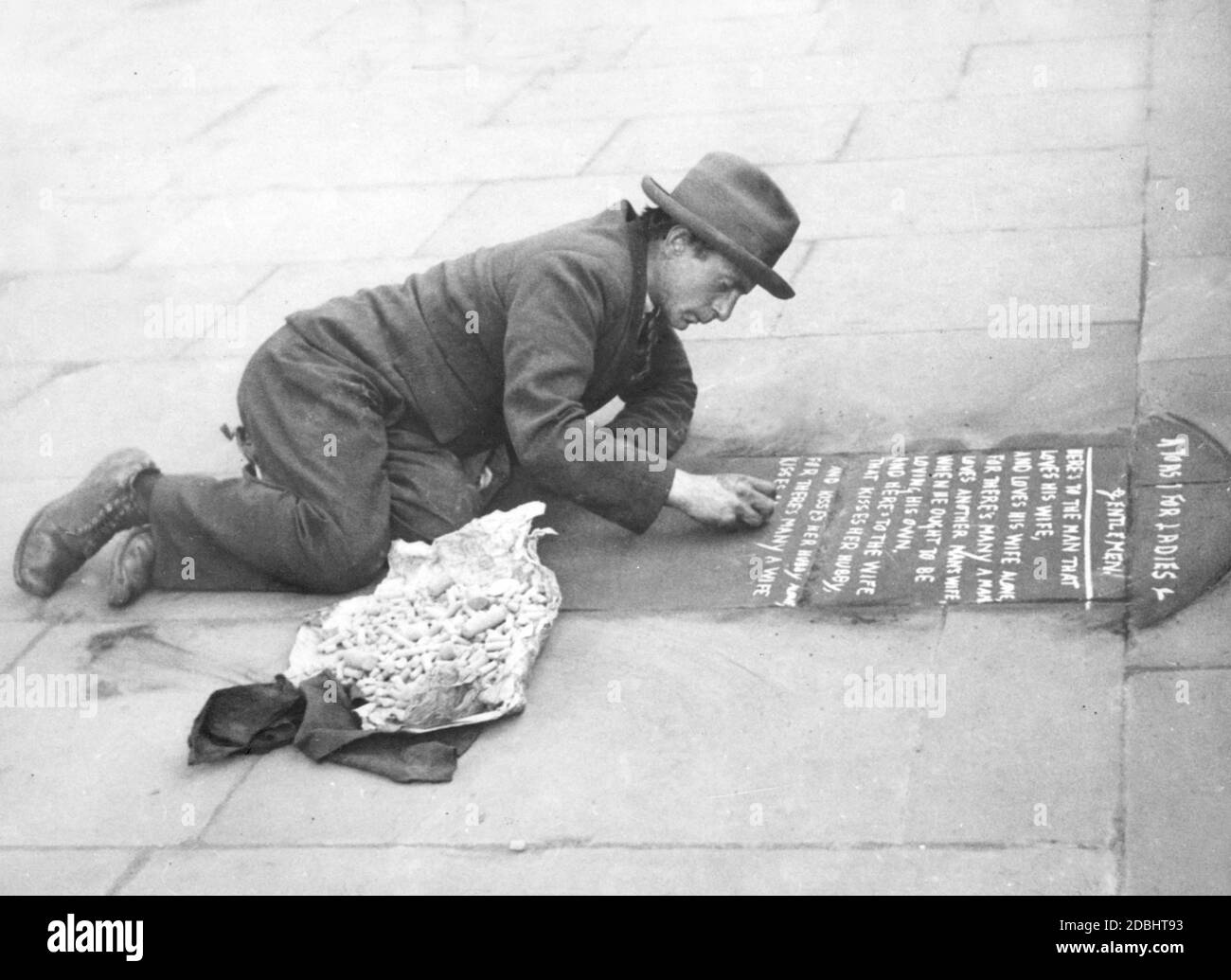 Un uomo disoccupato scrive versetti sul pavimento con gesso per guadagnare qualcosa. Foto Stock