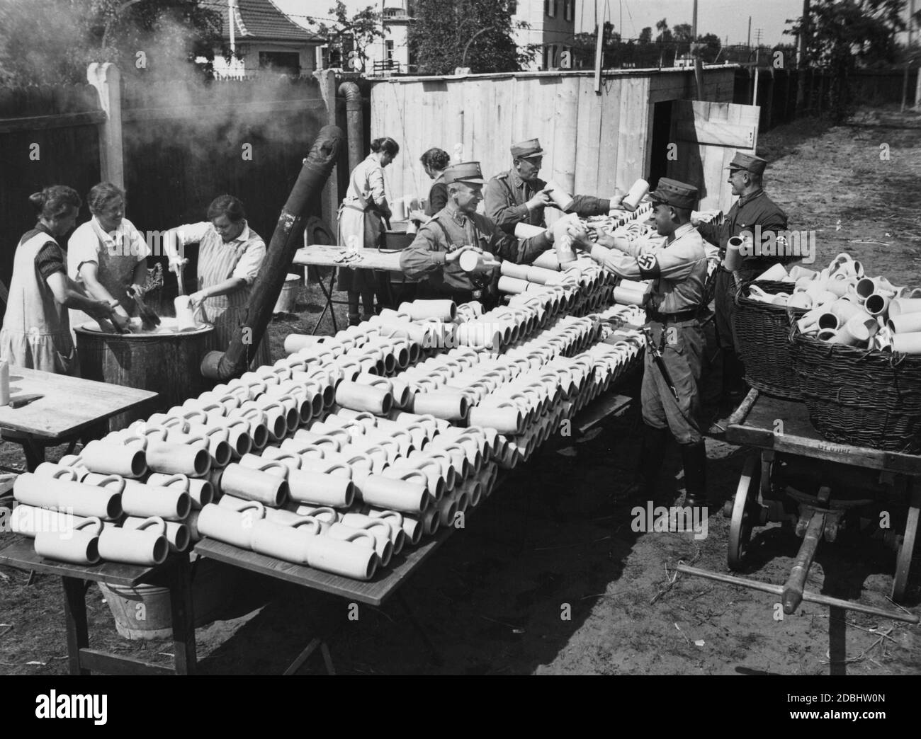 Le donne risciacquano le tazze in grandi botti, mentre gli uomini della SA in uniforme trasportano le tazze ai luoghi di dispiegamento con l'aiuto di un carrello, in modo che i partecipanti del Congresso del Partito nazista a Norimberga non soffrono di sete. Foto Stock