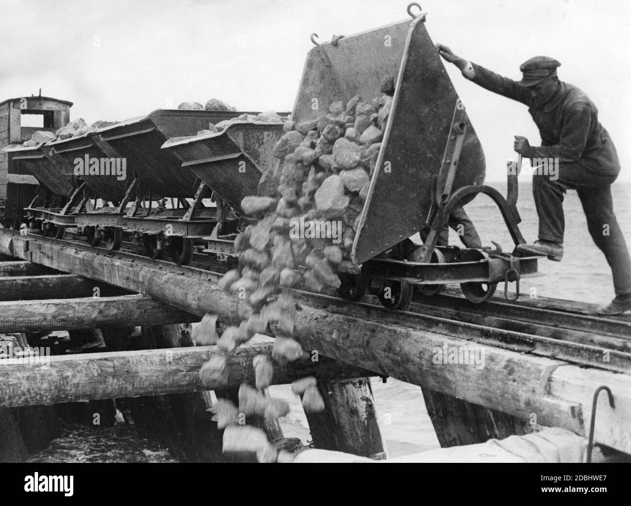 Un operaio costruisce una diga e scarica pietre da un camion nel mare. (foto non datata) Foto Stock
