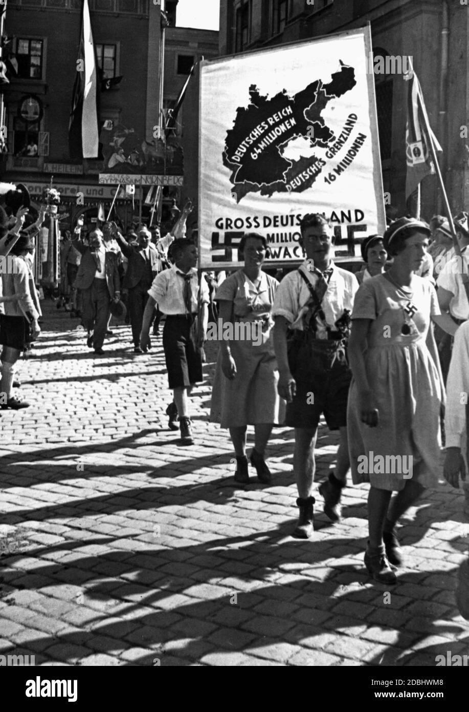 "I partecipanti alla parata in occasione della conferenza VDA di Passau portano con sé un banner sul quale sono raffigurati il Reich tedesco e il ''confine tedesco'', con le cifre della popolazione di 64 milioni e 16 milioni. Sotto di essa, tra due swastikas, si trova l'iscrizione ''Greater Germany. 80 milioni di svegli». Dietro la bandiera c'è una delegazione del Gymnasium Alte di Norimberga. In primo piano una donna indossa una swastika come decorazione. Sul bordo sinistro della foto c'è un gruppo di uomini in costume tradizionale.' Foto Stock