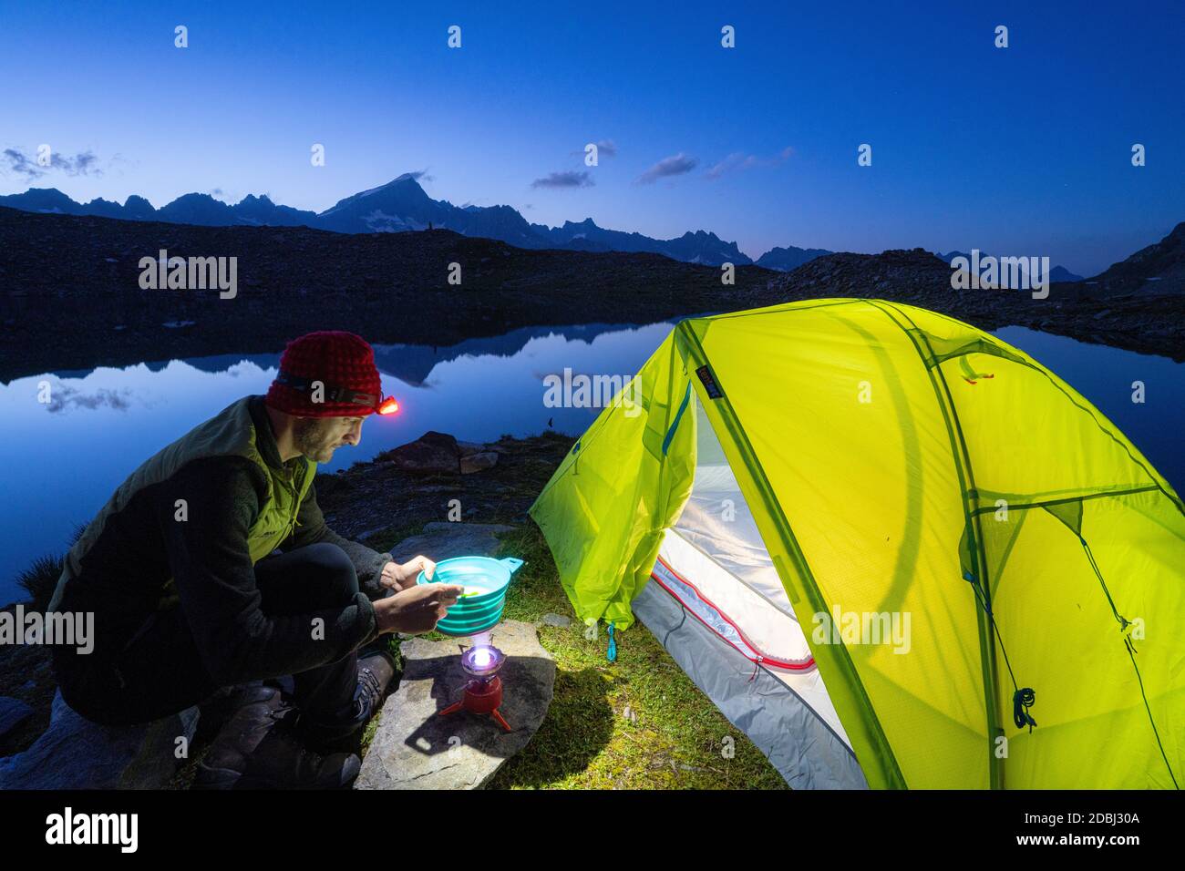 Escursionista uomo cucina fuori tenda campeggio al lago Obere Schwarziseeli al crepuscolo, Passo Furka, Canton Uri, Svizzera, Europa Foto Stock