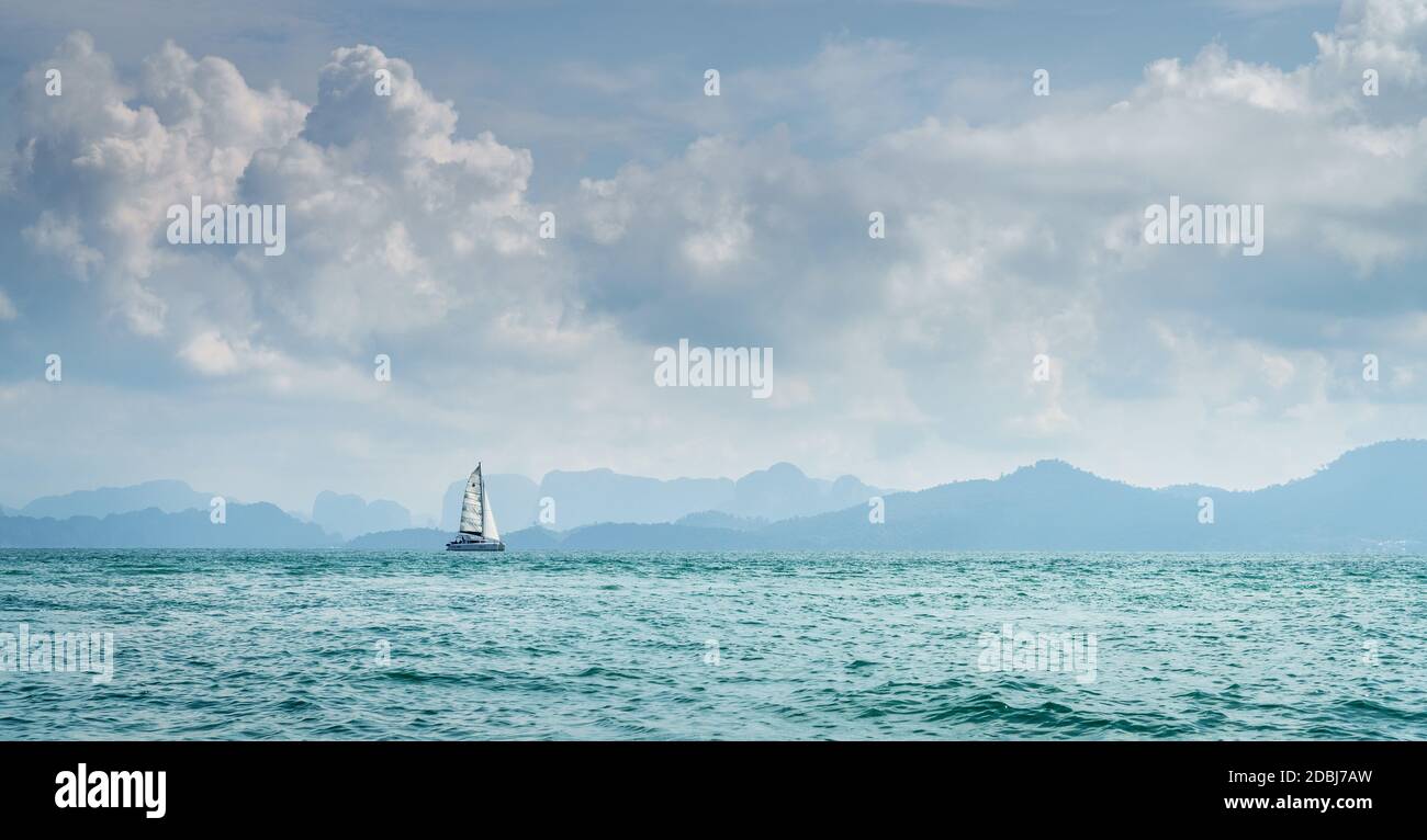 Lone barca a vela nel Mare delle Andamane in Thailandia con la costa di Krabi all'orizzonte Foto Stock