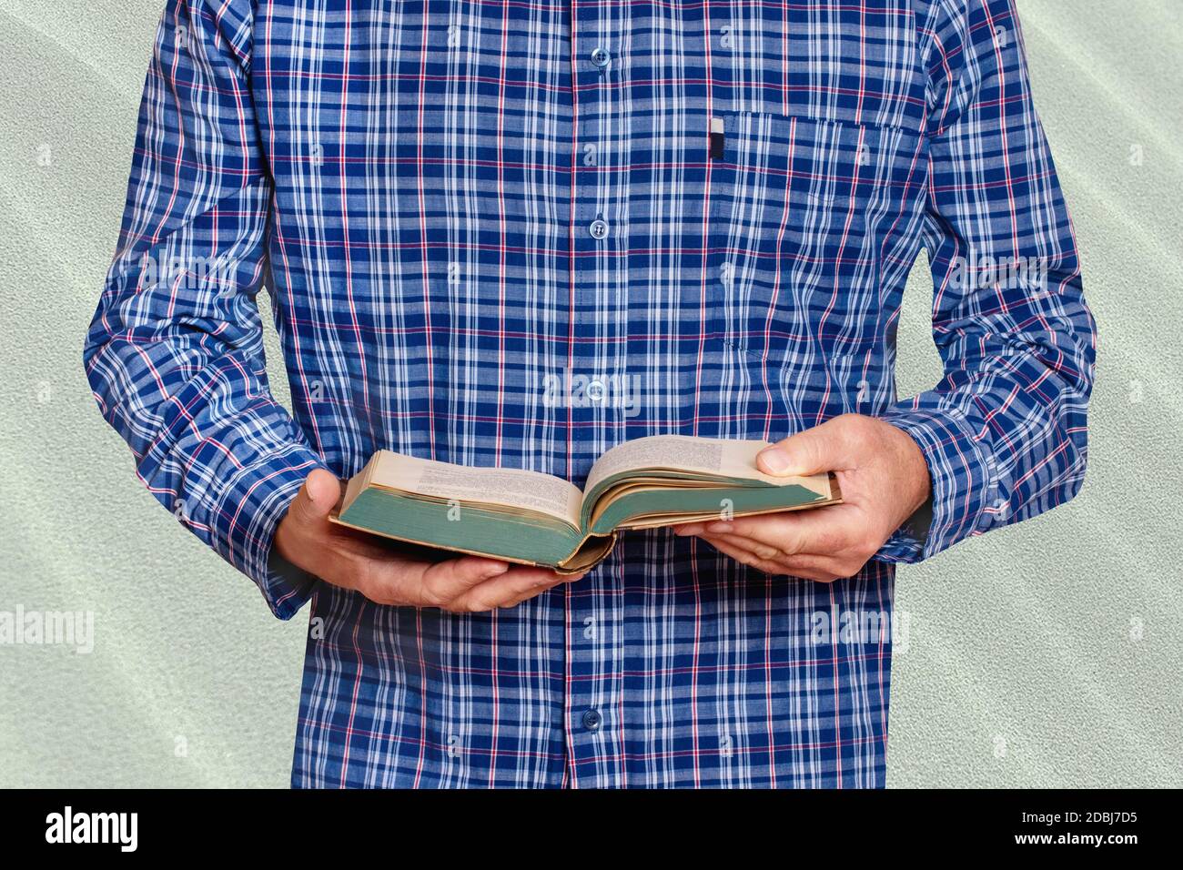 La closeup delle mani di un uomo in una camicia a righe blu e bianca tiene un vecchio libro nelle sue mani e legge. Uomo d'affari di fronte a un muro di pietra luminoso. Mac Foto Stock