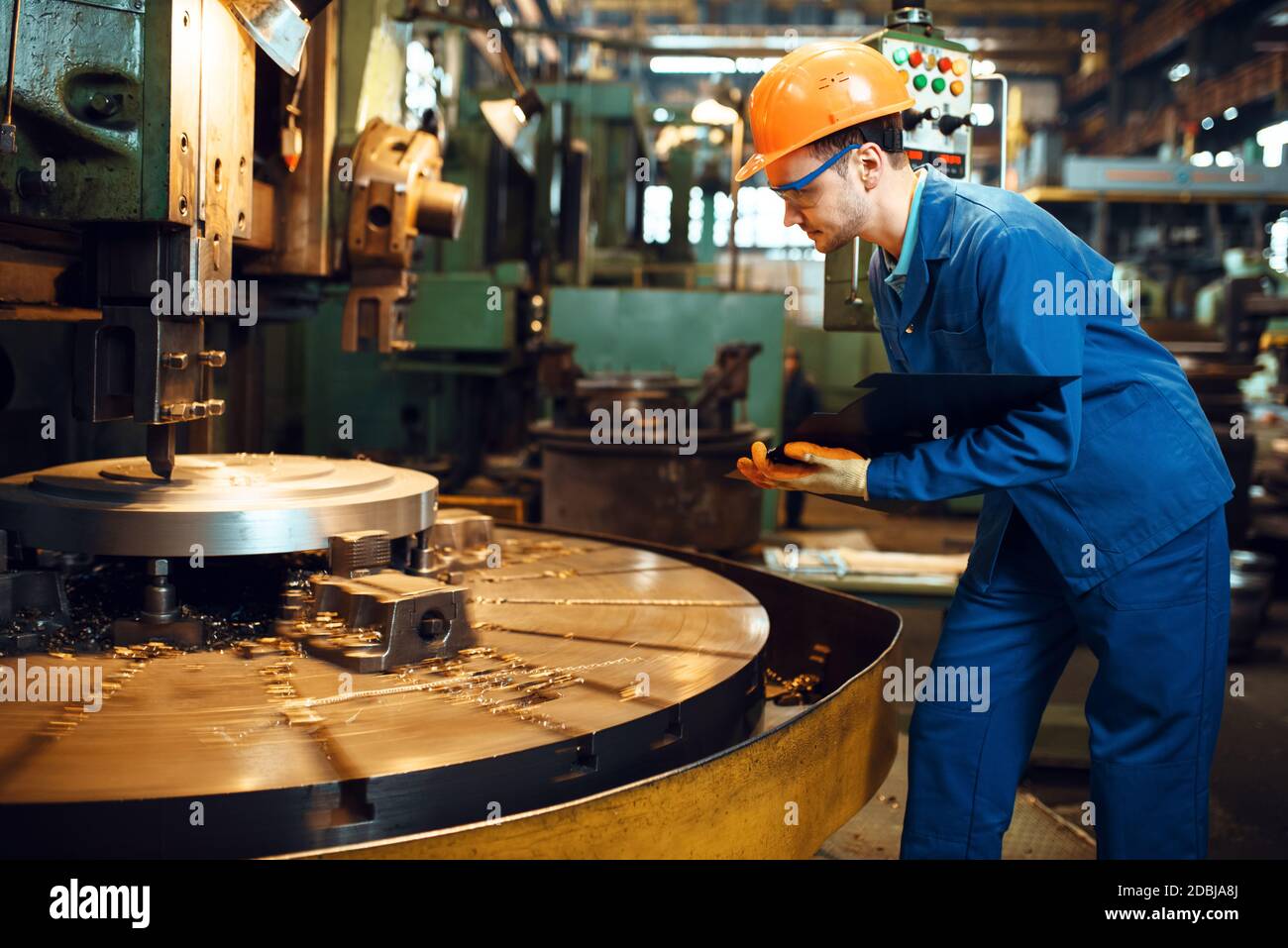 Turner in uniforme e casco stanging presso il tornio automatico, fabbrica. Produzione industriale, ingegneria metallurgica, produzione Foto Stock