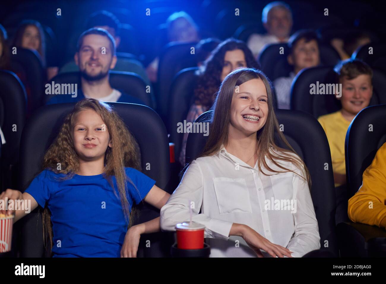 Ritratto di ragazza che guarda il film con la sorella più giovane nel  cinema, ridendo con i denti, dentisti bretelle. Allegro caucasico femmina  adolescente indossare camicia godere di film con la famiglia.